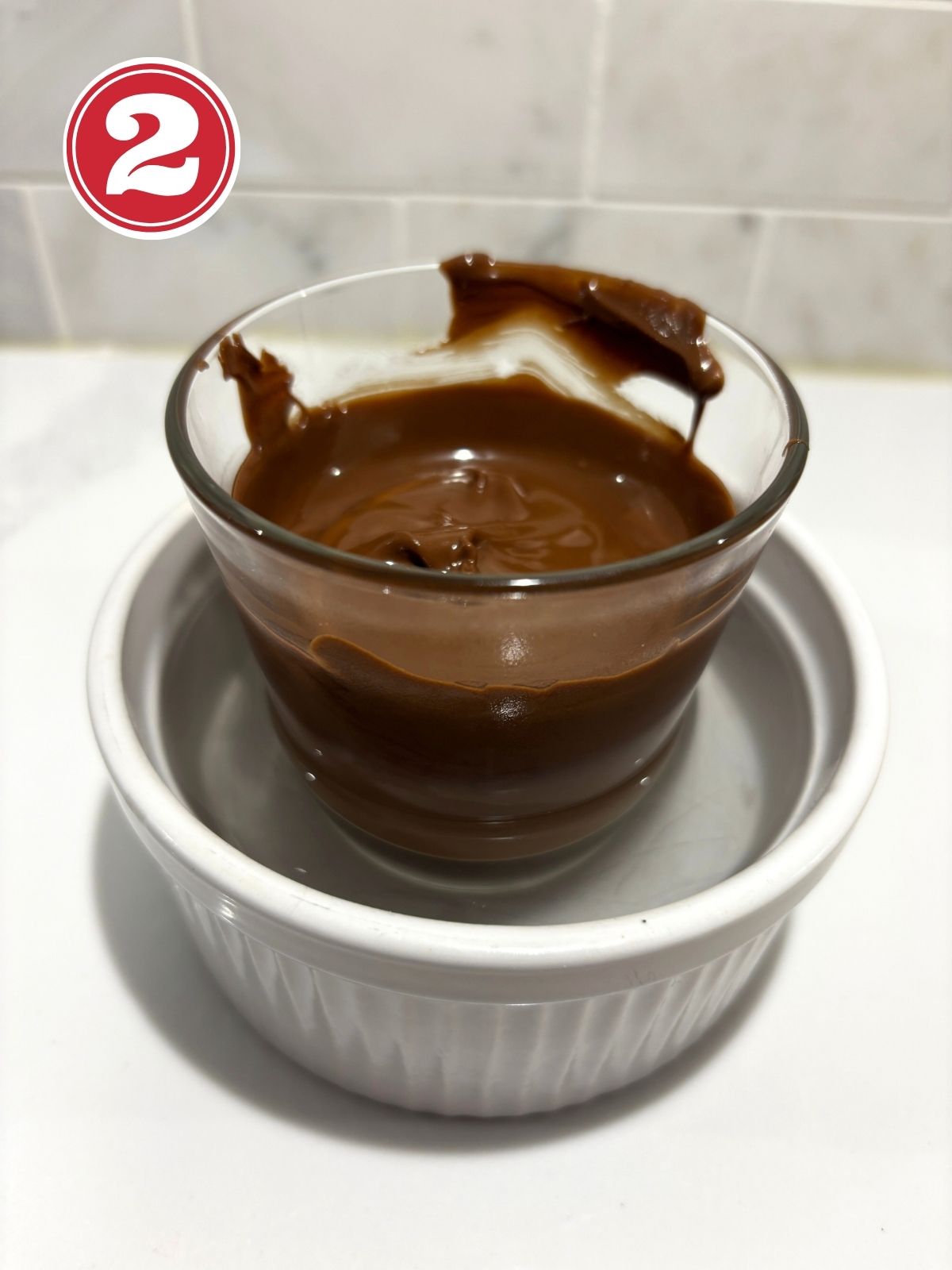 melted chocolate in a glass sitting in a ramekin filled with hot water