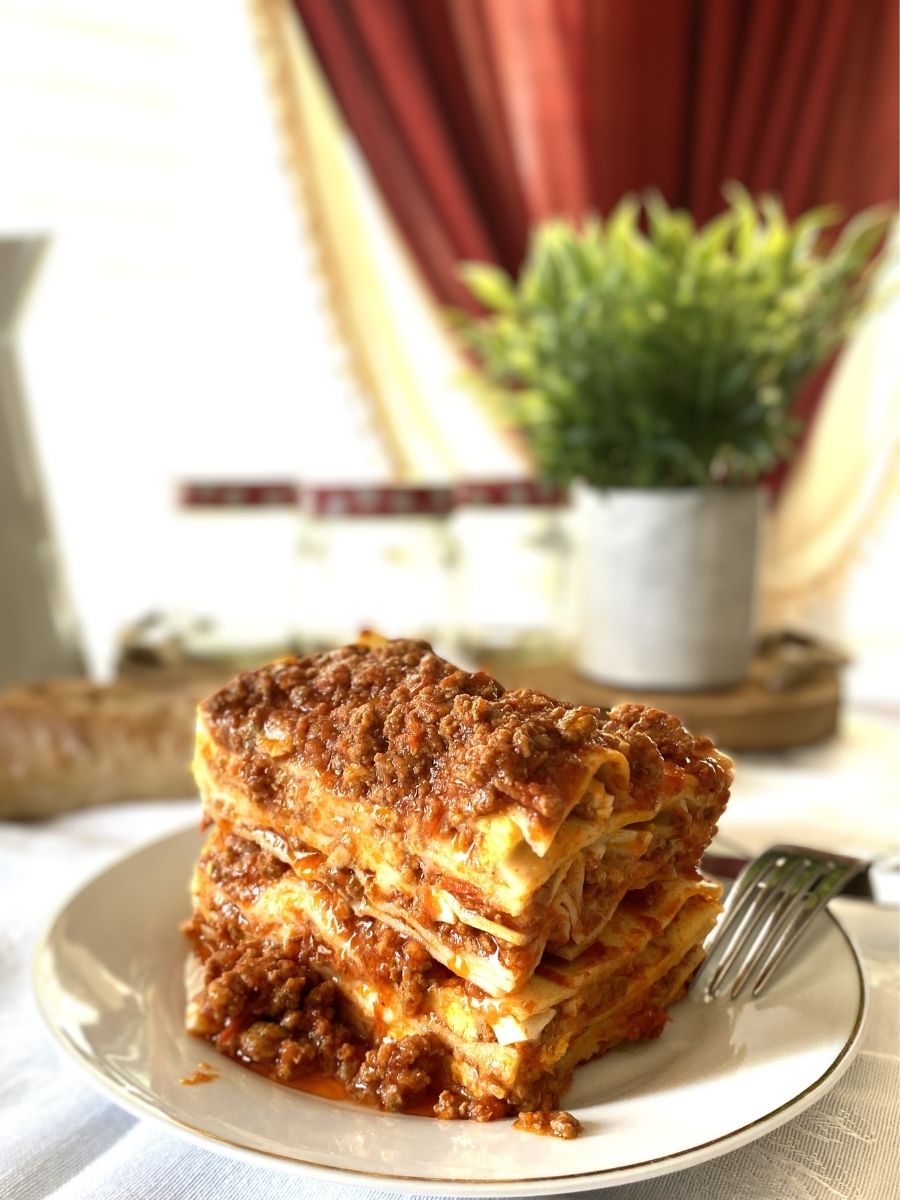 Lasagna al Forno in a white plate with curtain in background
