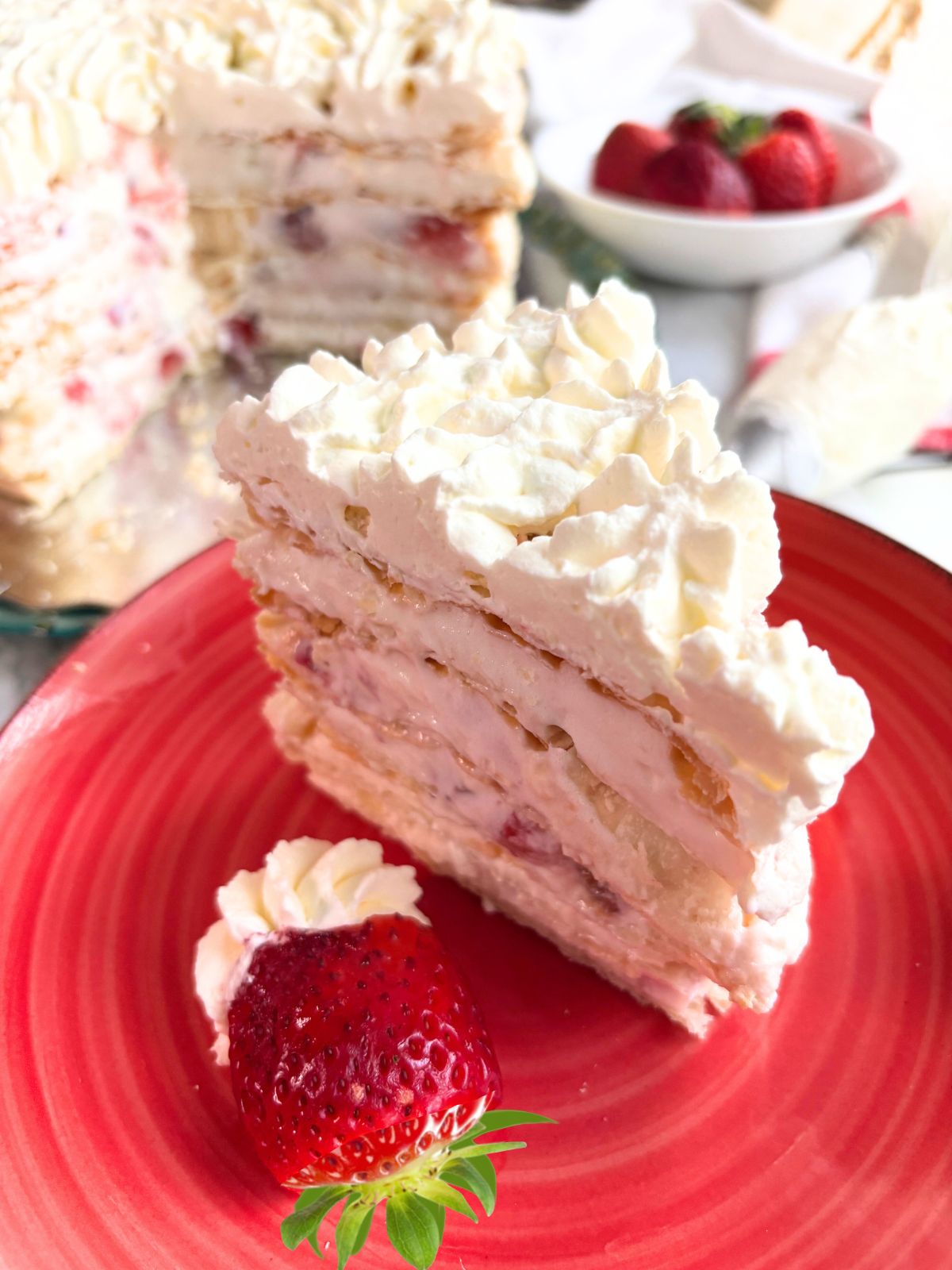 Strawberry Sfoglia Cake slice in a red plate with strawberry and whipped cream in plate