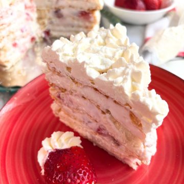 Strawberry Sfoglia Cake slice in a red plate with strawberry and whipped cream in plate