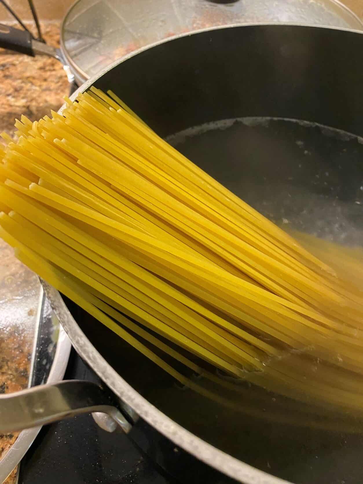 raw spaghetti in boiling water in a black pot