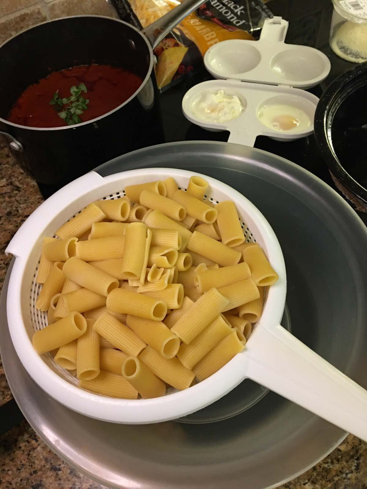 Rigatoni pasta in a white colander eggs in the background