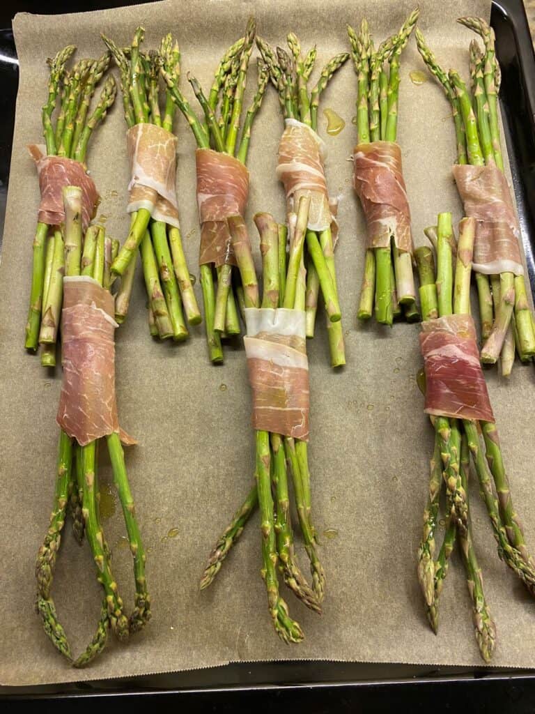Asparagus wrapped in prosciutto on a baking sheet