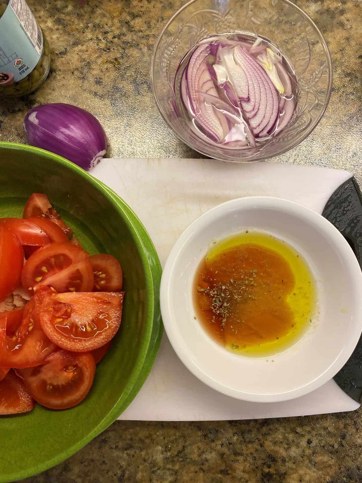 tomatoes, onion and salad dressing on a cutting board