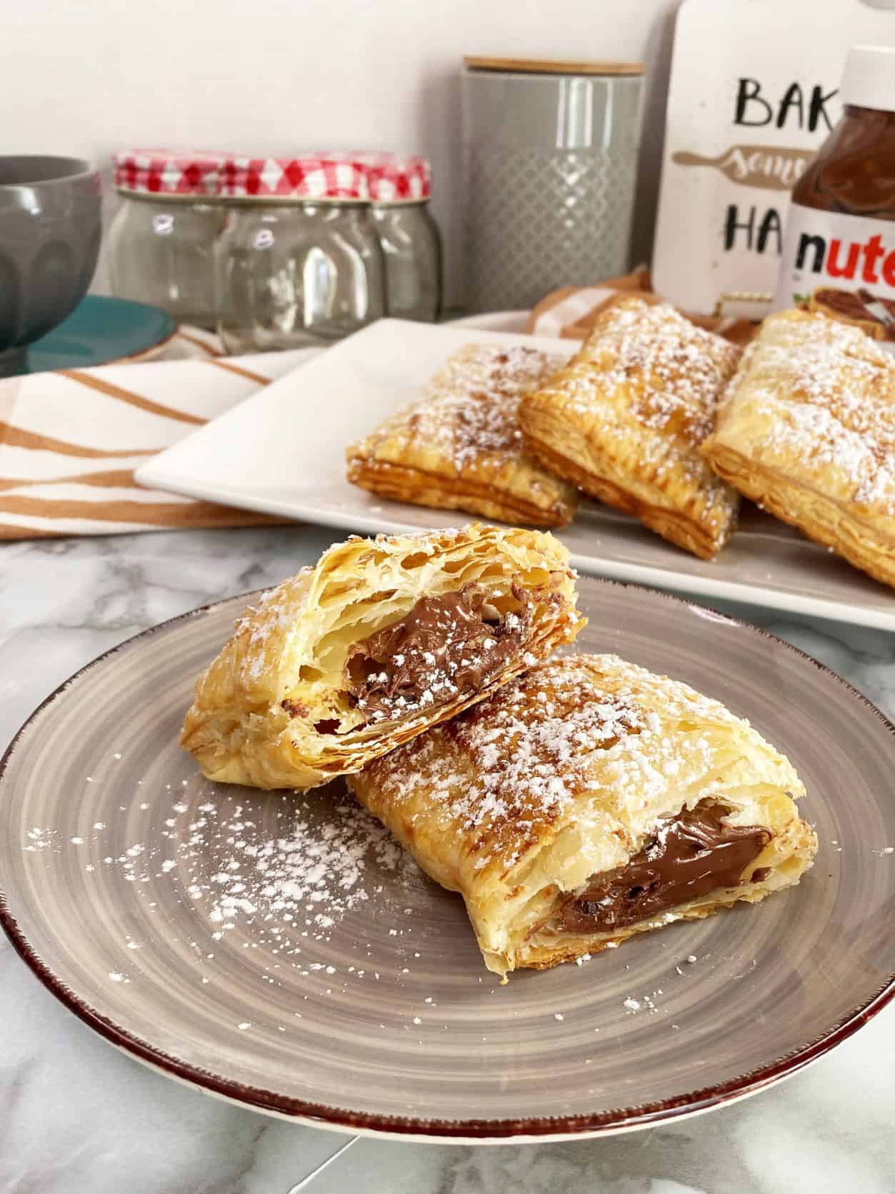Nutella Puff pastry turnovers in a grey plate infront of tray of turnovers