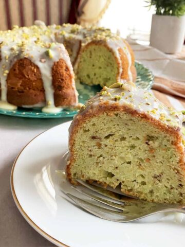 A slice of pistachio cake in a plate with Cake in background