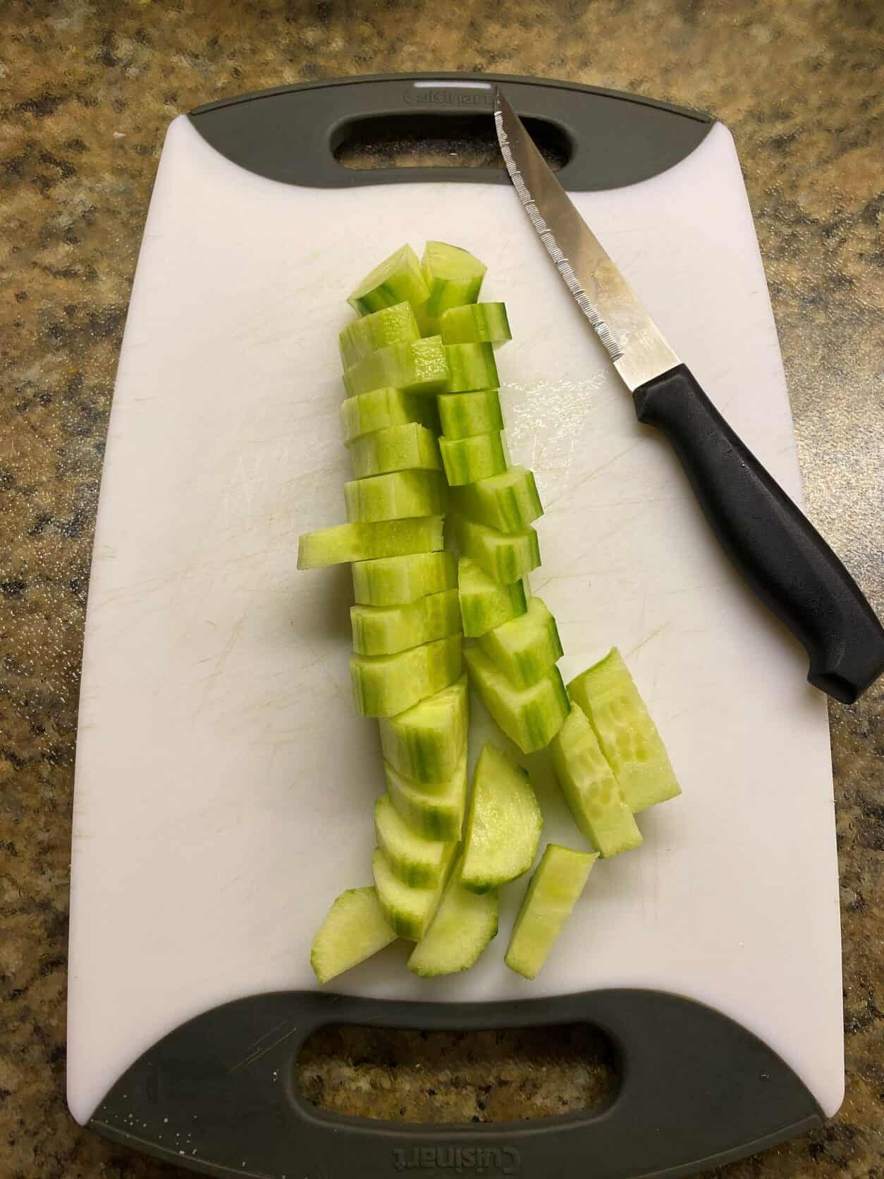 peeled and sliced cucumber on a white cutting board