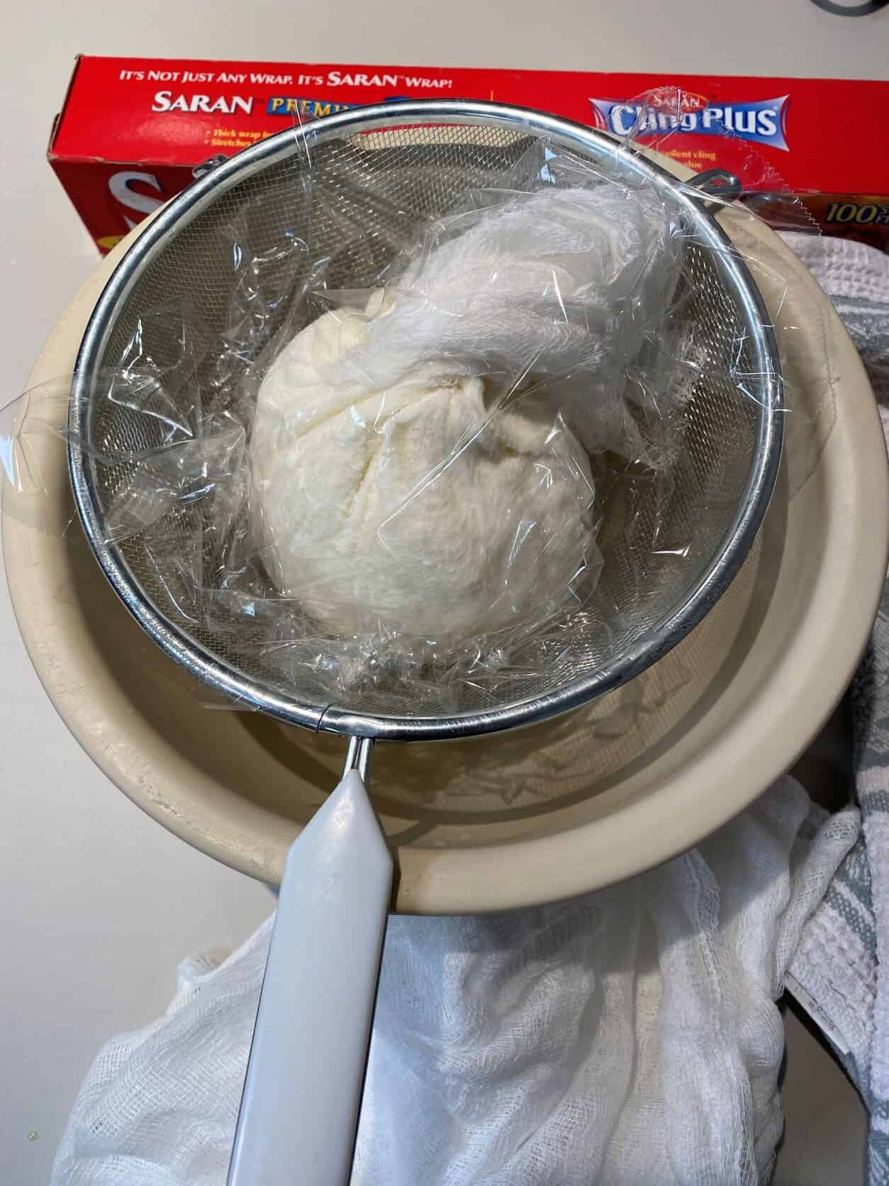 ricotta in cheese cloth over strainer and bowl