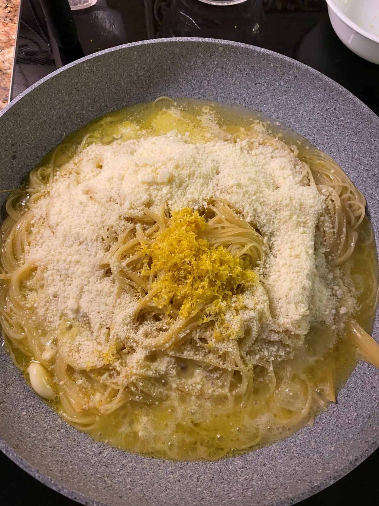 adding cheese, grated lemon and lemon juice to pasta in a skillet