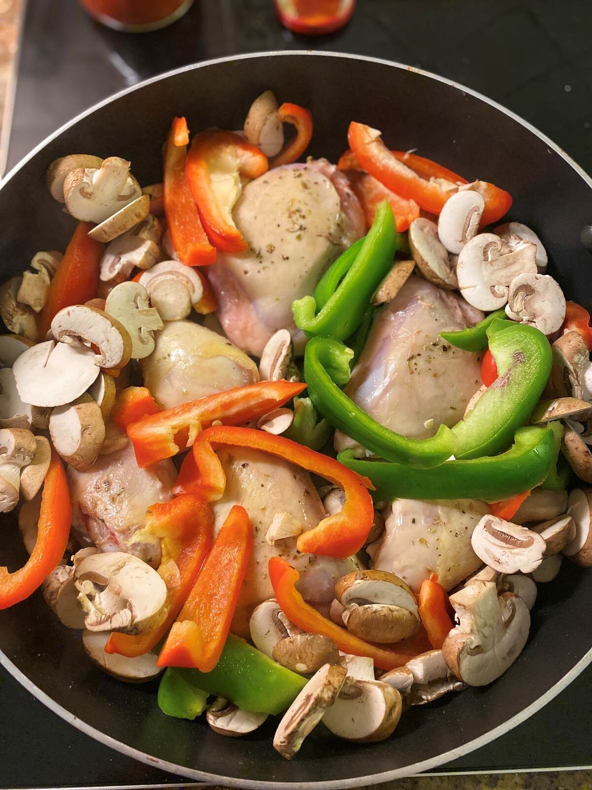 Chicken legs thighs with peppers and mushrooms in a skillet