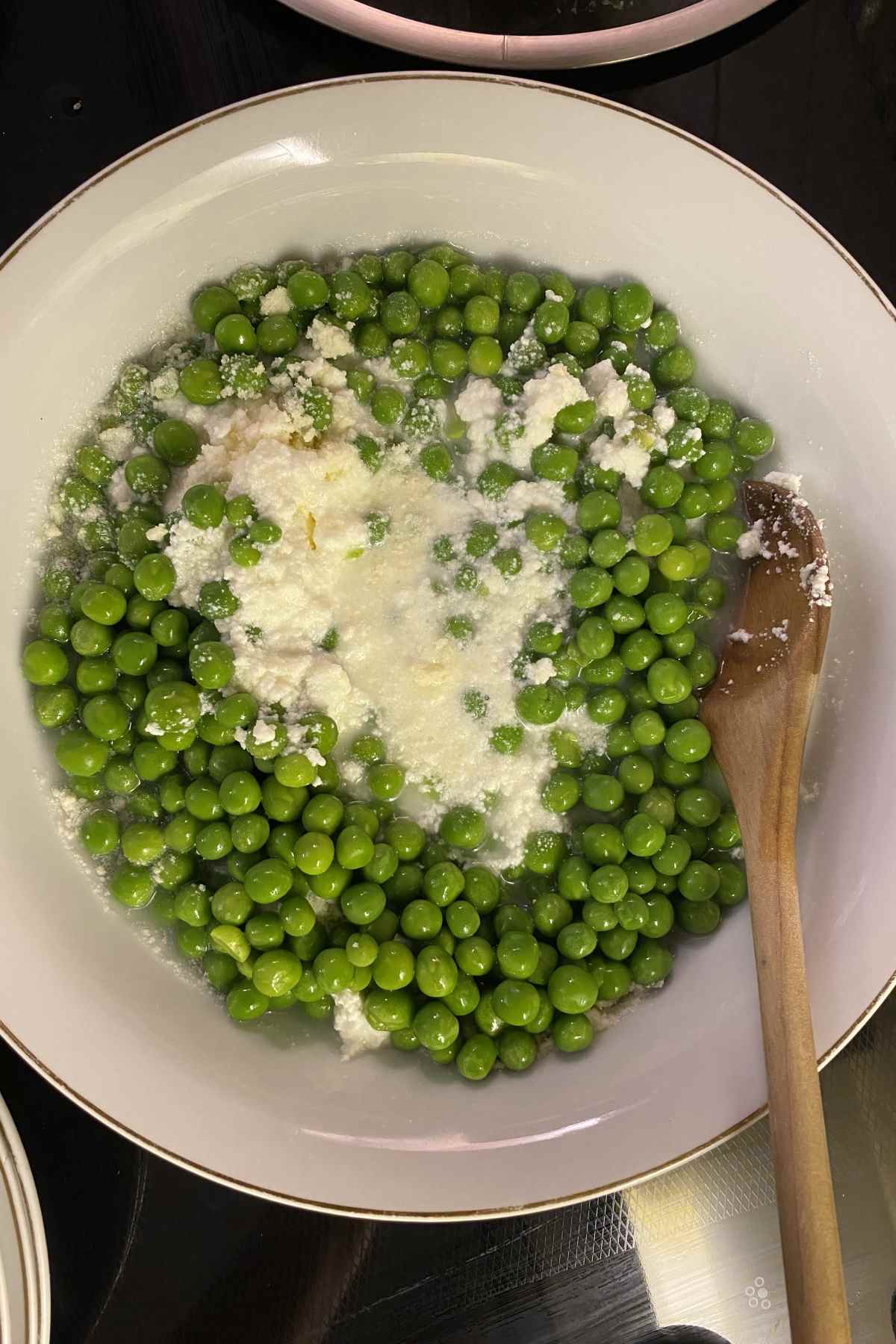 Peas, ricotta and parmesan cheese in a white bowl with a wooden spoon