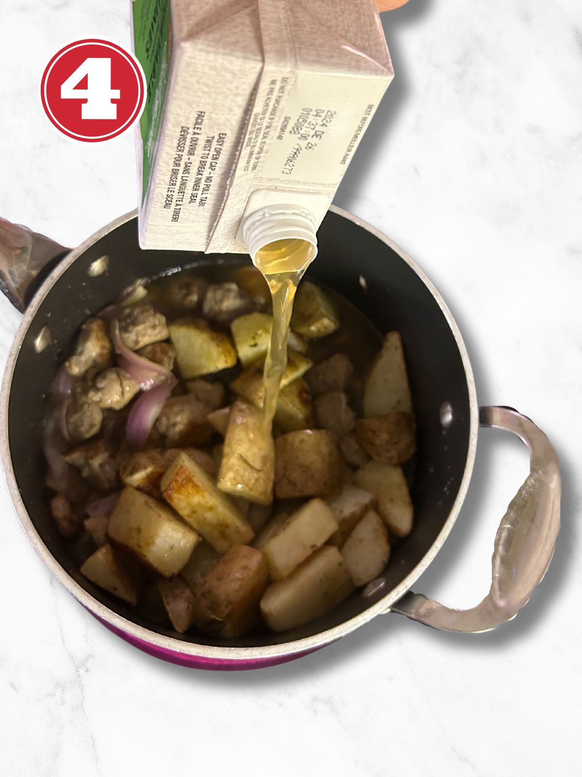 potatoes and sausage and onions in a pot, adding broth