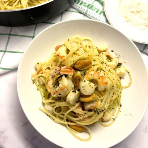 A vibrant bowl of seafood pasta featuring shrimp and herbs in a light white wine sauce.