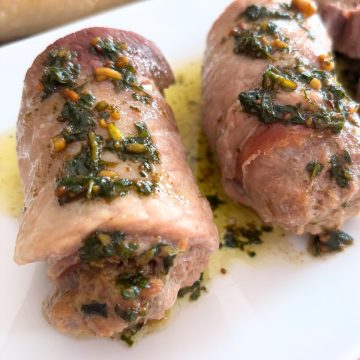 Pork Braciole in a white plate drizzled with Pesto Sauce
