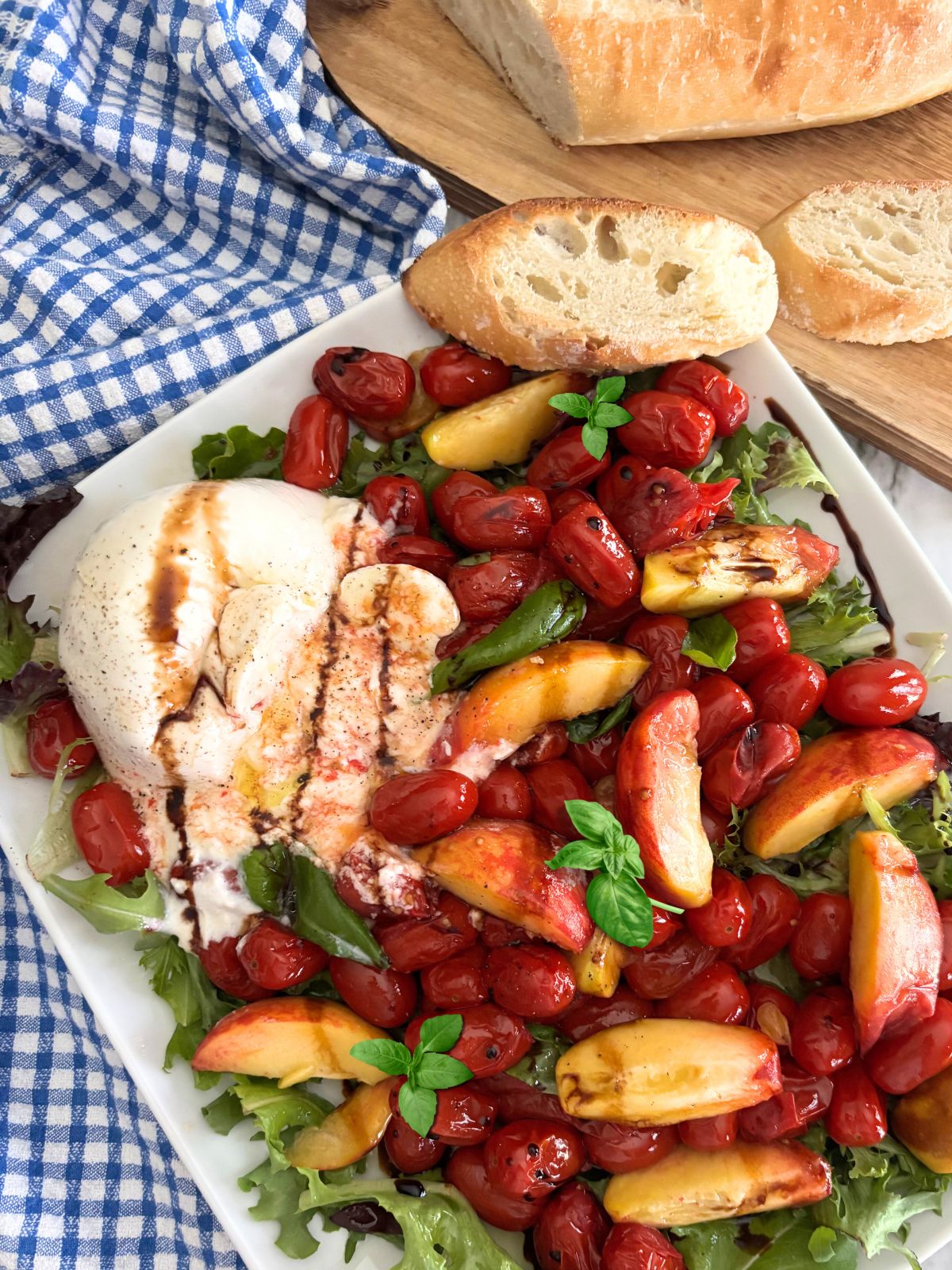 Peach burrata Salad in a white plate with crusty bread on the side
