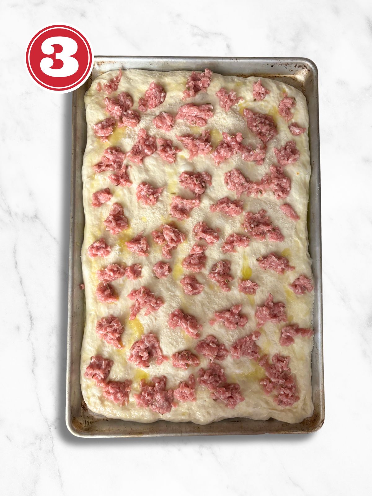 pizza dough in an aluminum pizza tray topped with sausage