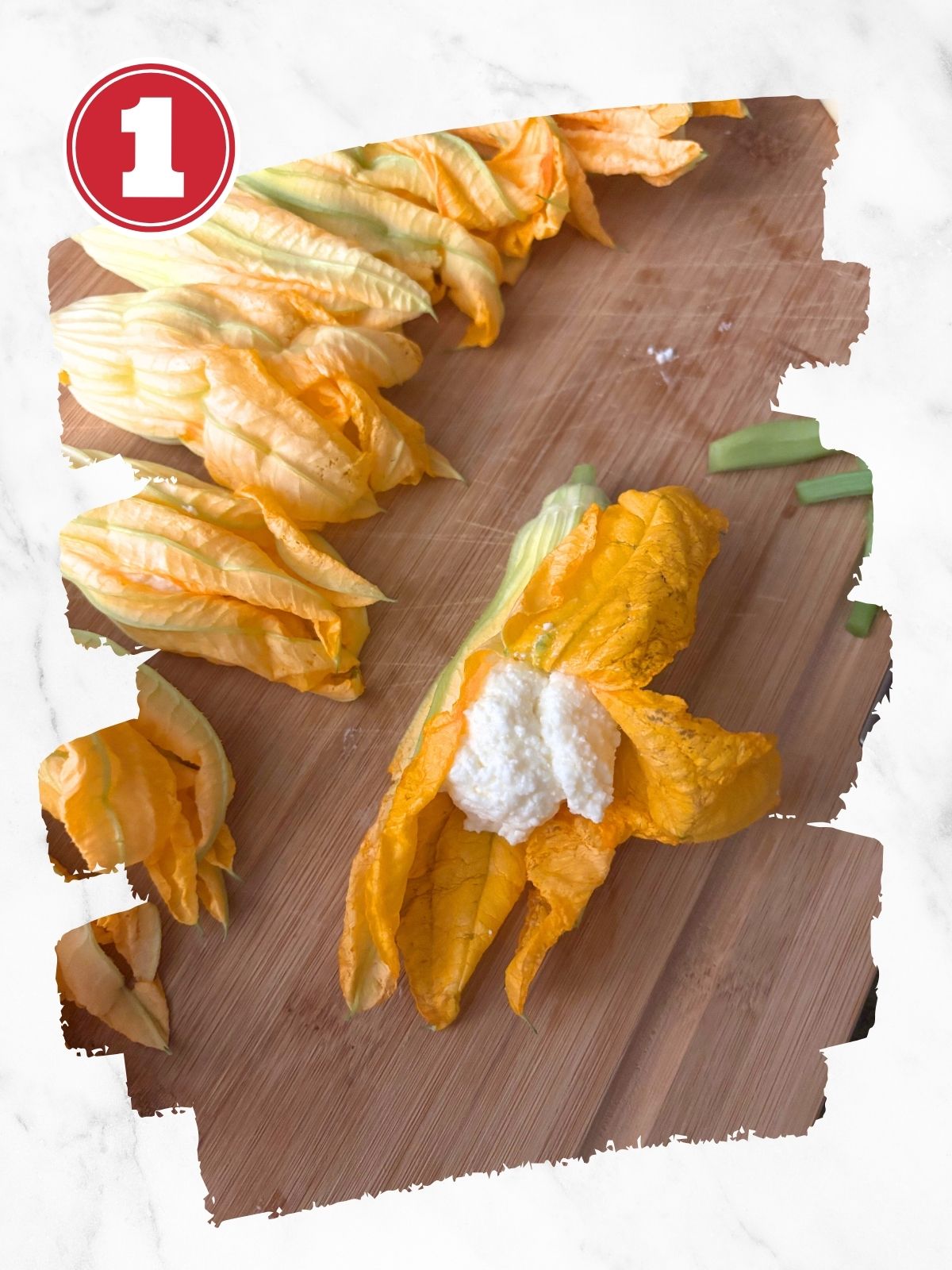 clean zucchini flowers on a wooden cutting board, one stuffed with cheese filling