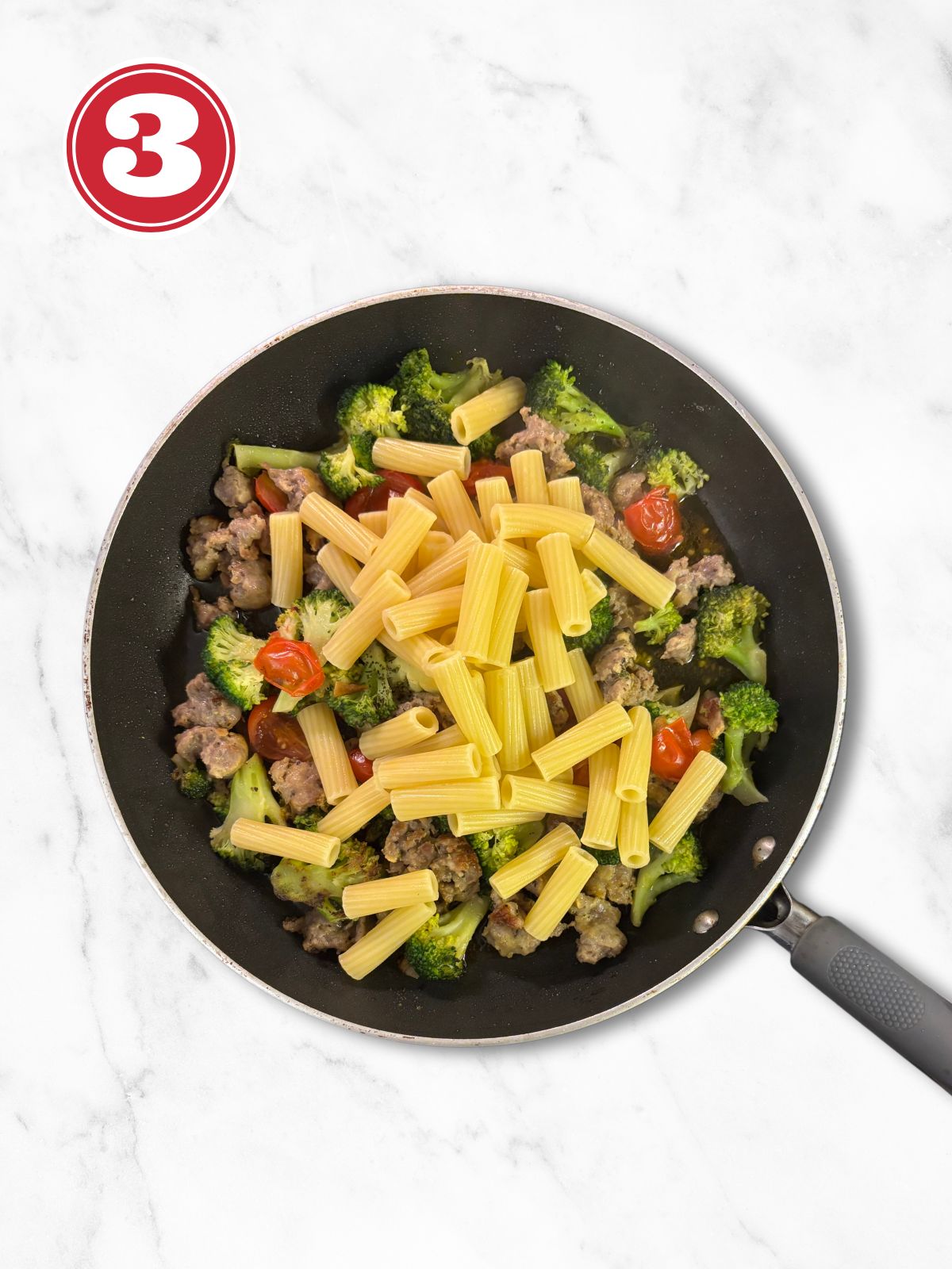 adding pasta to broccoli and sausage in a skillet