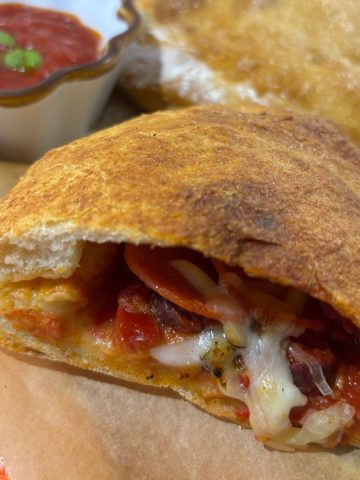 sliced in half calzone on parchment paper, tomato sauce in background