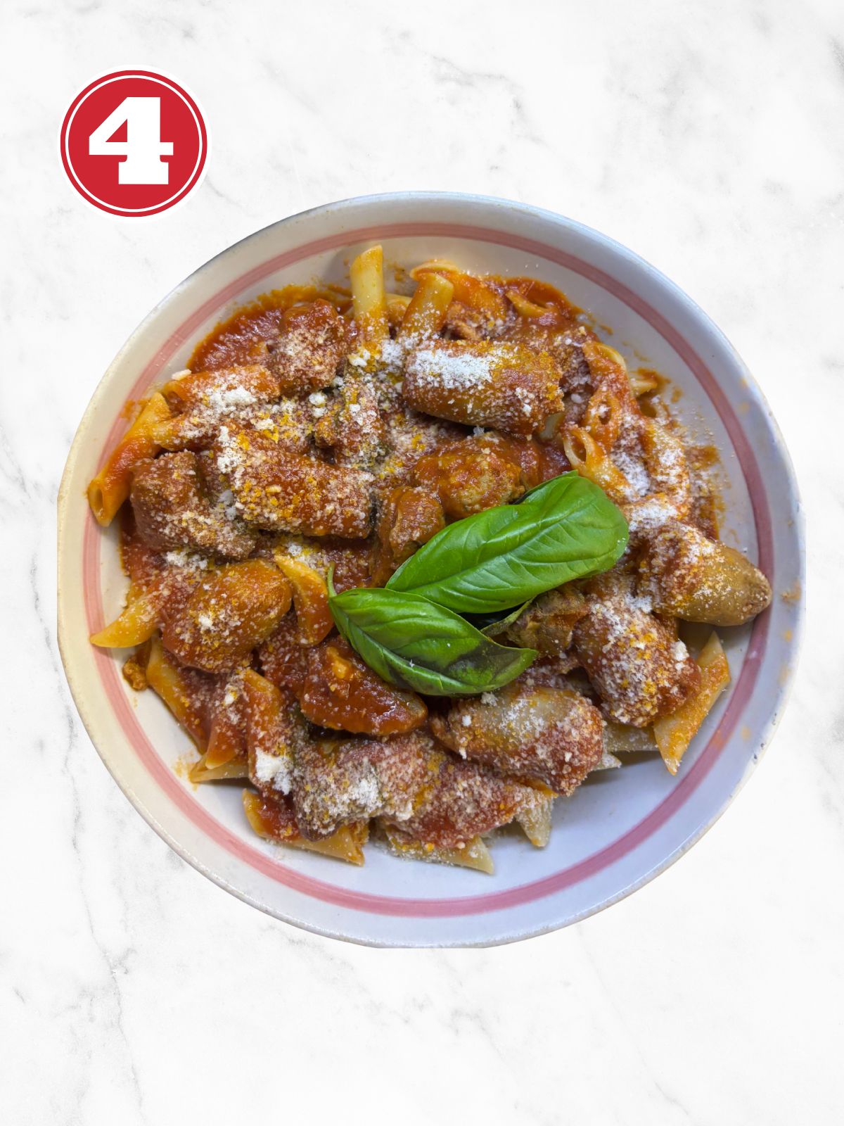 Penne Pasta with Sunday Sauce in a white bow, parmesan and a 2 leaves of Basil
