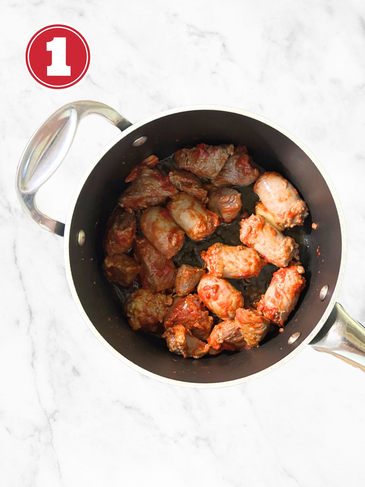 Sausage and beef stewing meat in a skillet with tomato paste